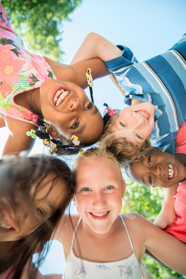 Kids and counselors form a circle while lying in the grass and smiling at camera.